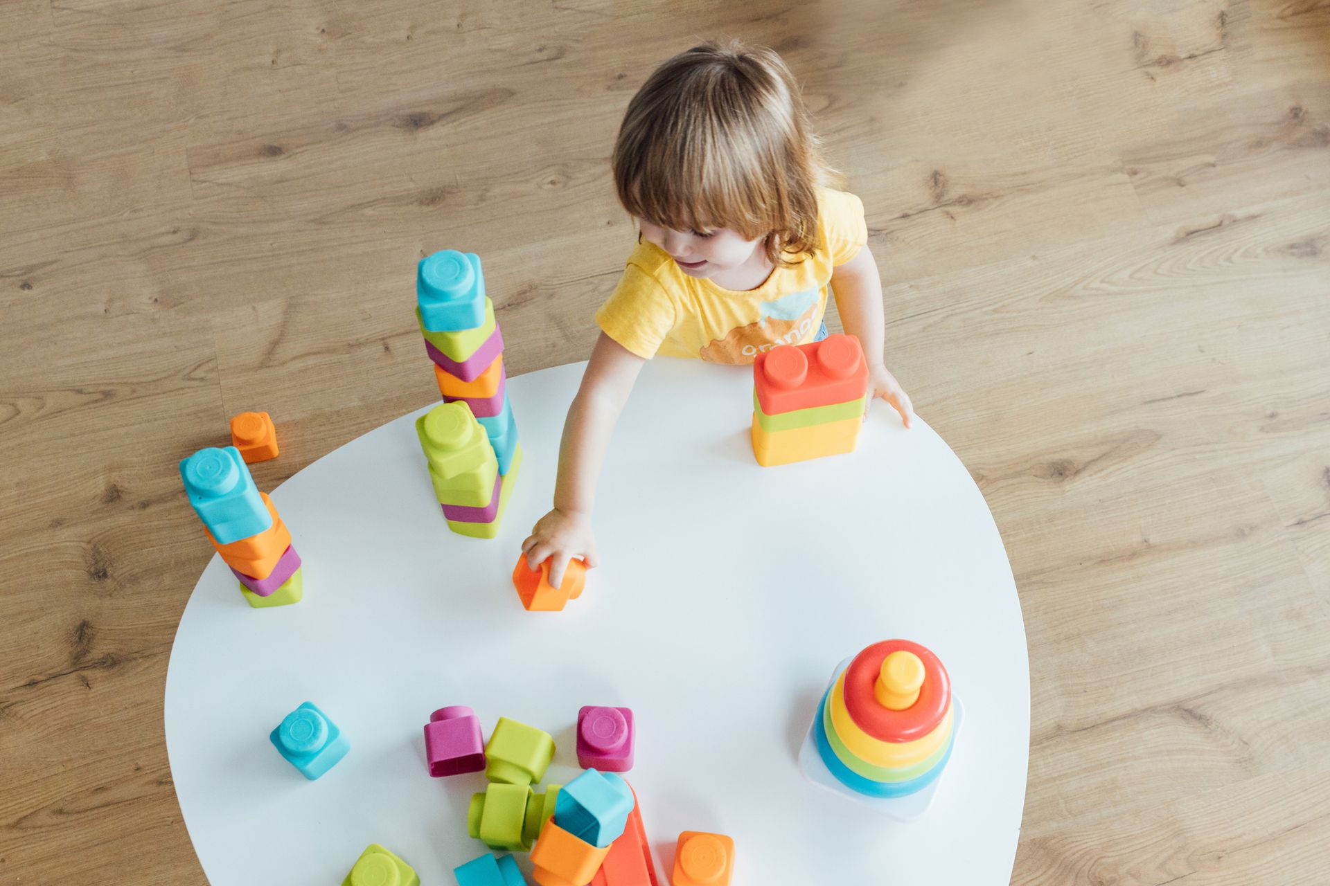 Bird's eye view of a little girl is playing with toy colored plastic blocks.