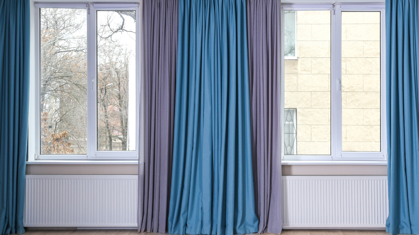 A woman is opening a window with blinds on it.