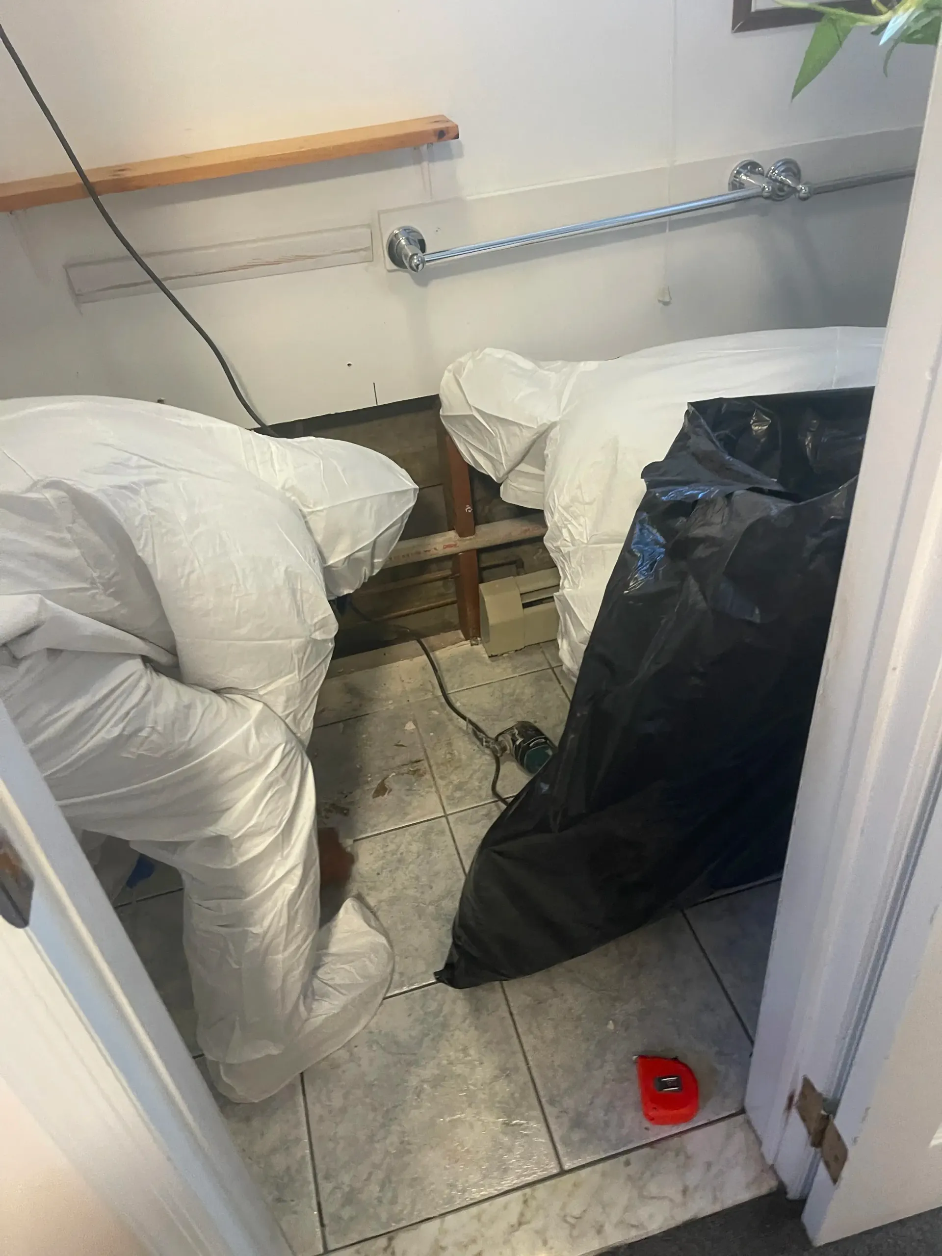 A restoration company man in a white suit is working on a bathroom floor.