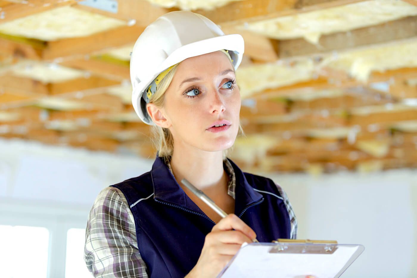 A man wearing a hard hat and goggles is writing on a clipboard