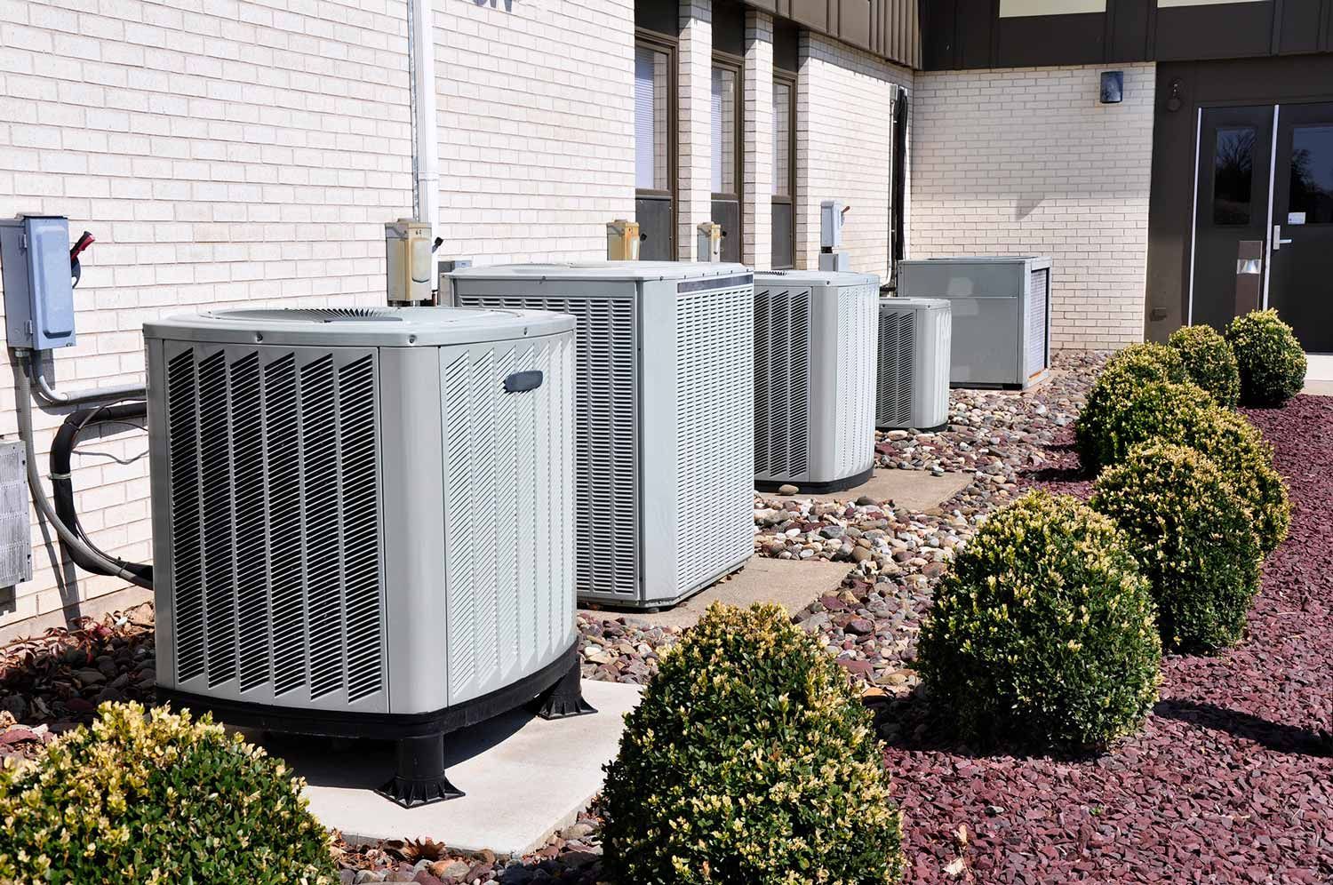A row of air conditioners are sitting outside of a building.