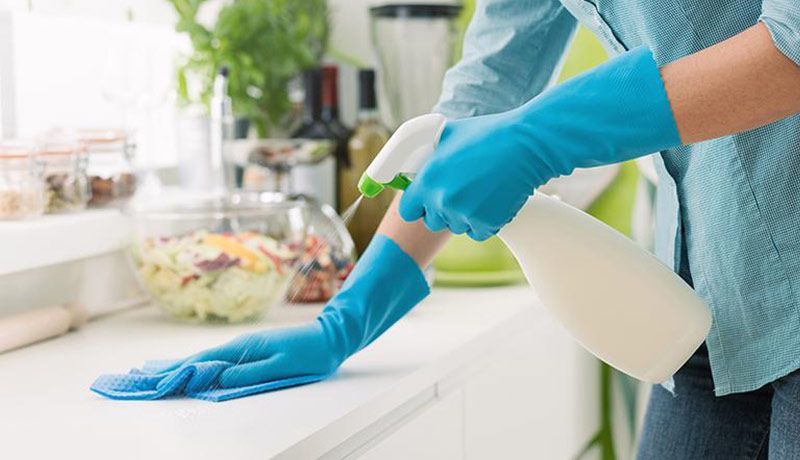 A person wearing blue gloves is cleaning a kitchen counter with a spray bottle.