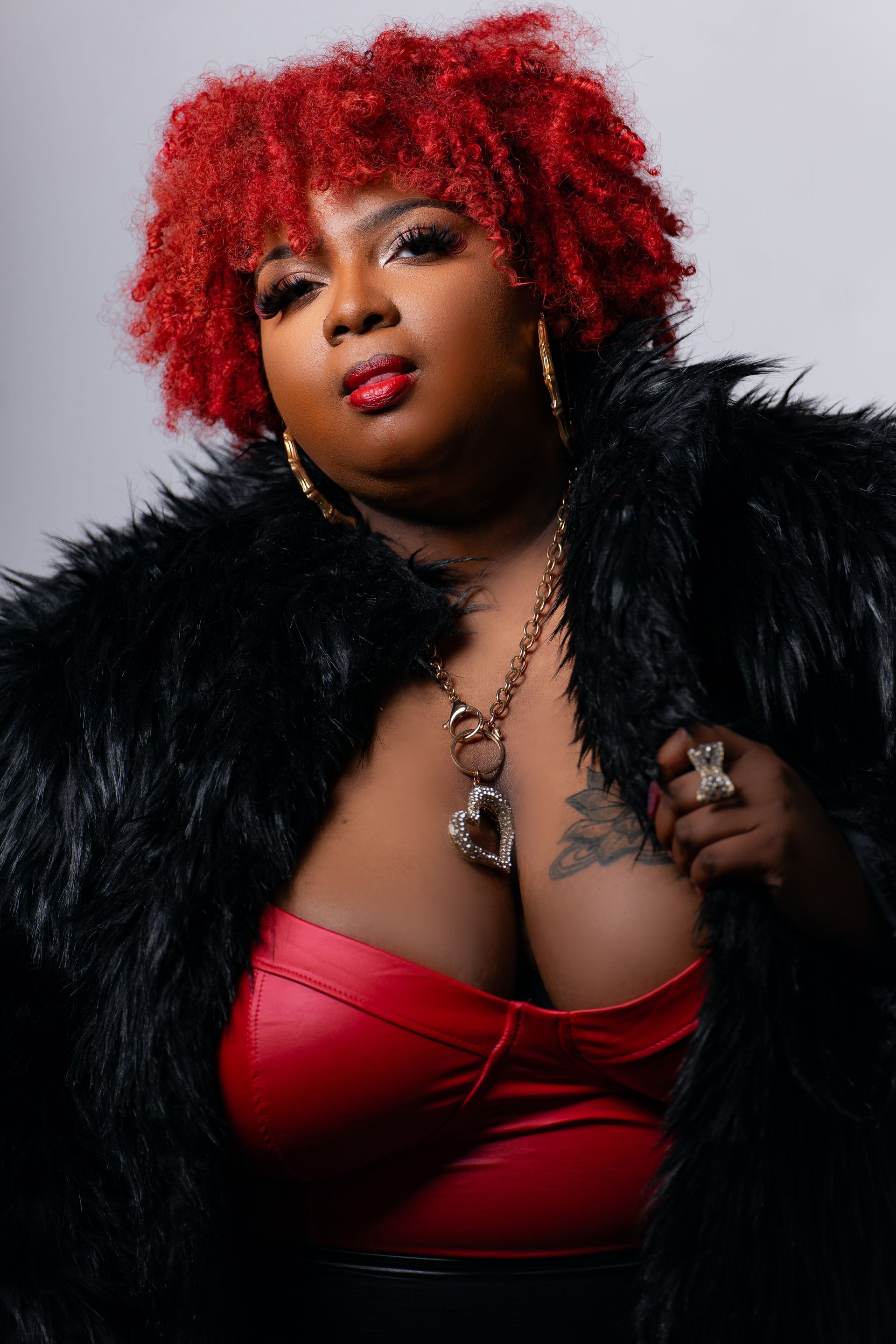 A woman with red hair is wearing a black fur coat and a red top.