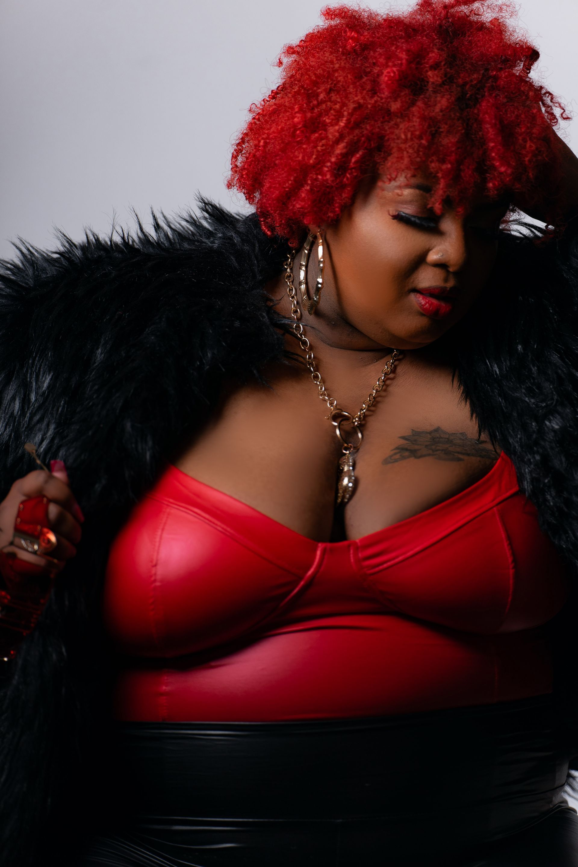 A woman with red hair is wearing a red bra and a black fur coat.