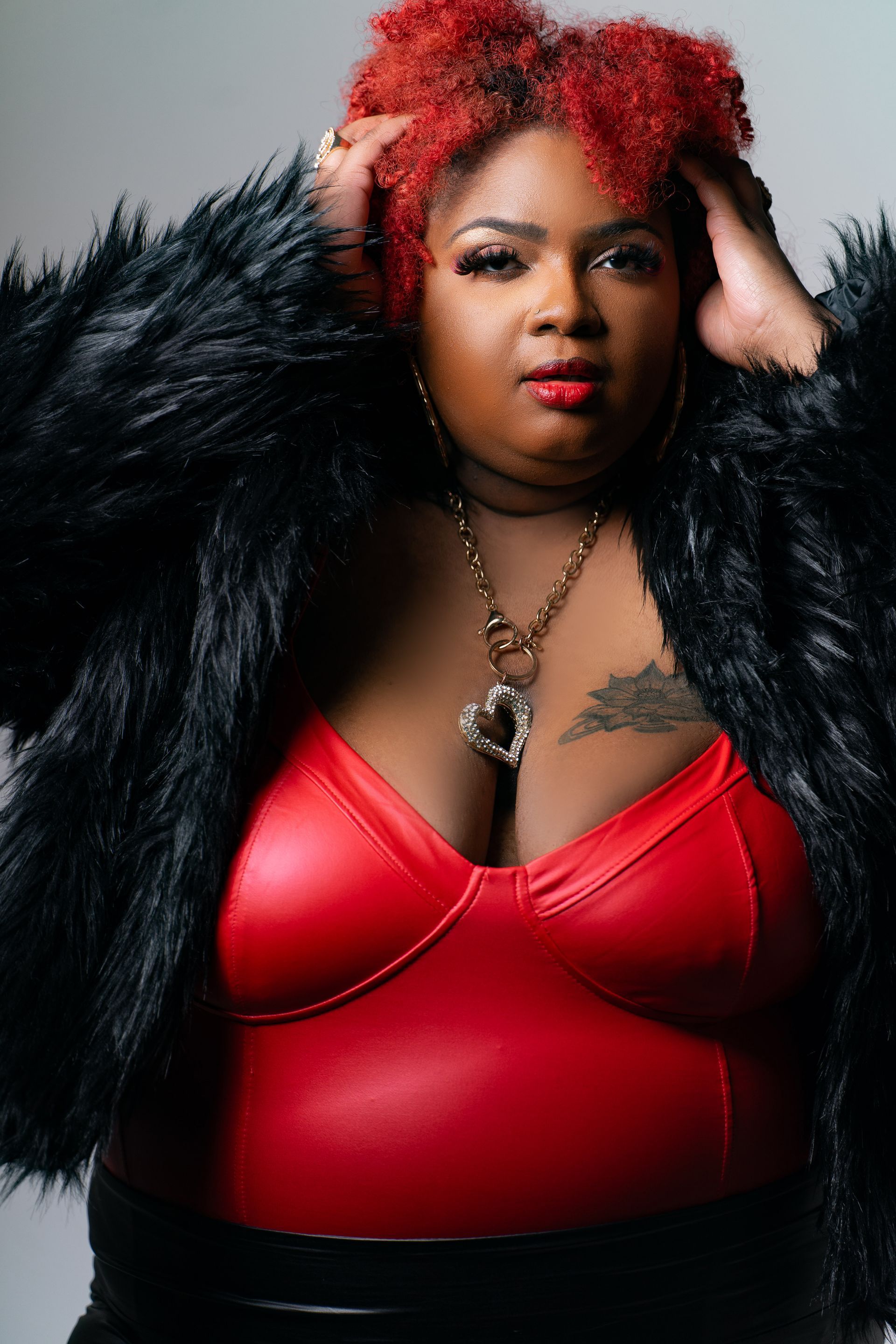 A woman with red hair is wearing a red bodysuit and a black fur coat.