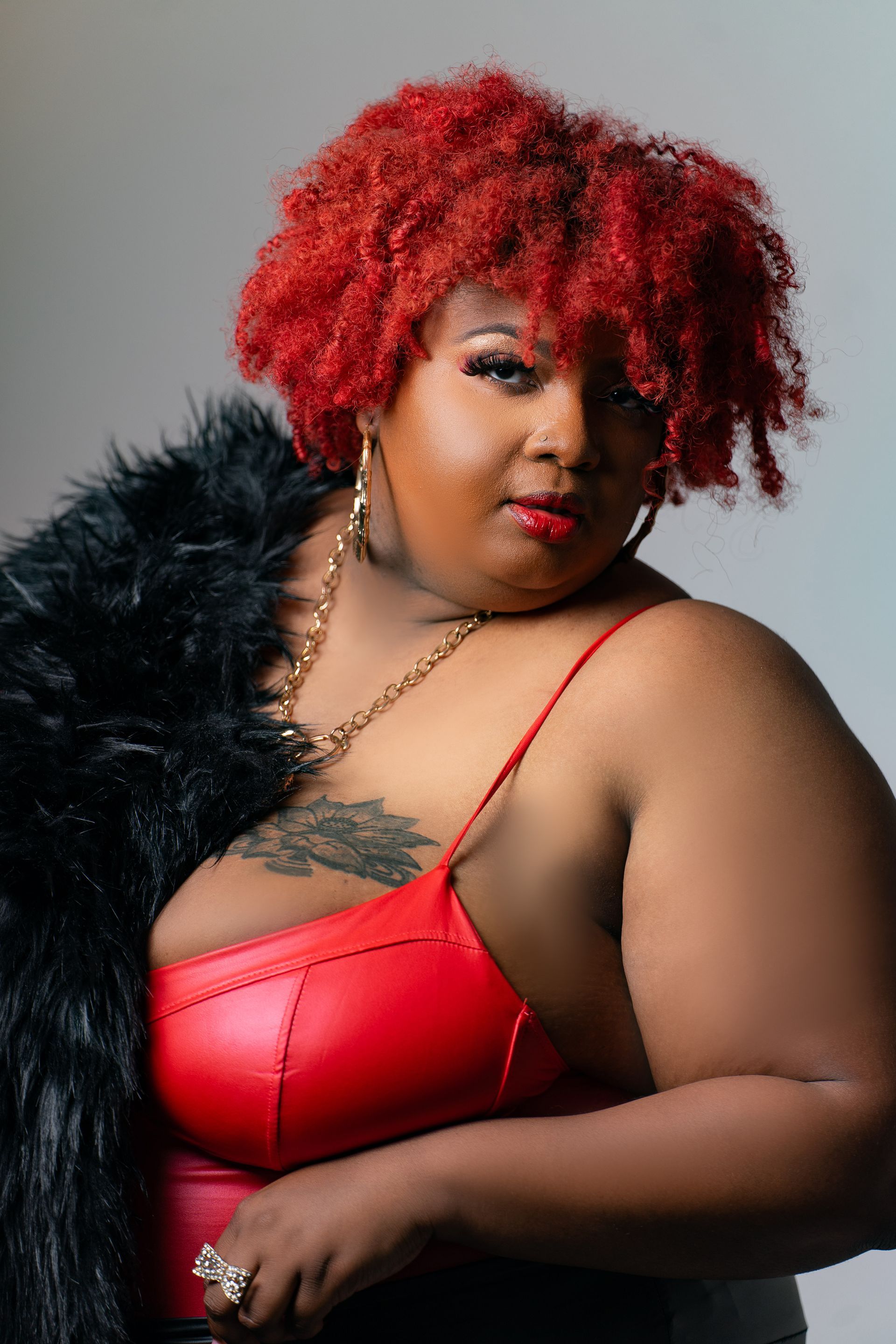 A woman with red hair is wearing a red bra and a black fur coat.