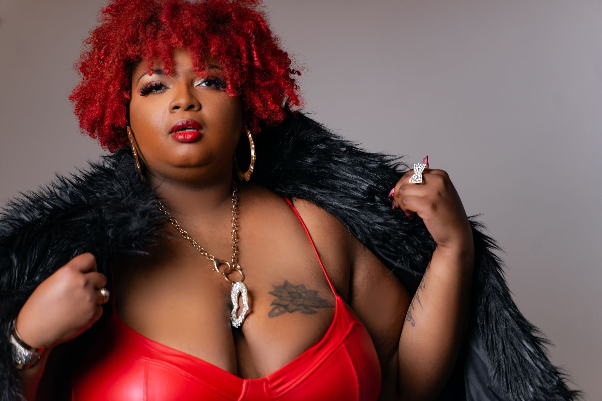 A woman with red hair is wearing a red bra and a black fur coat.