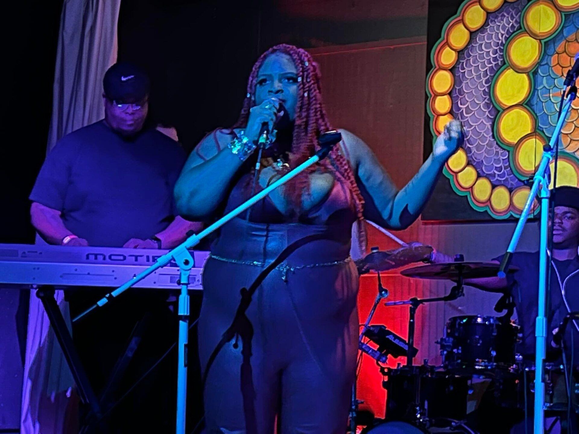 A woman is singing into a microphone on a stage in front of a keyboard.