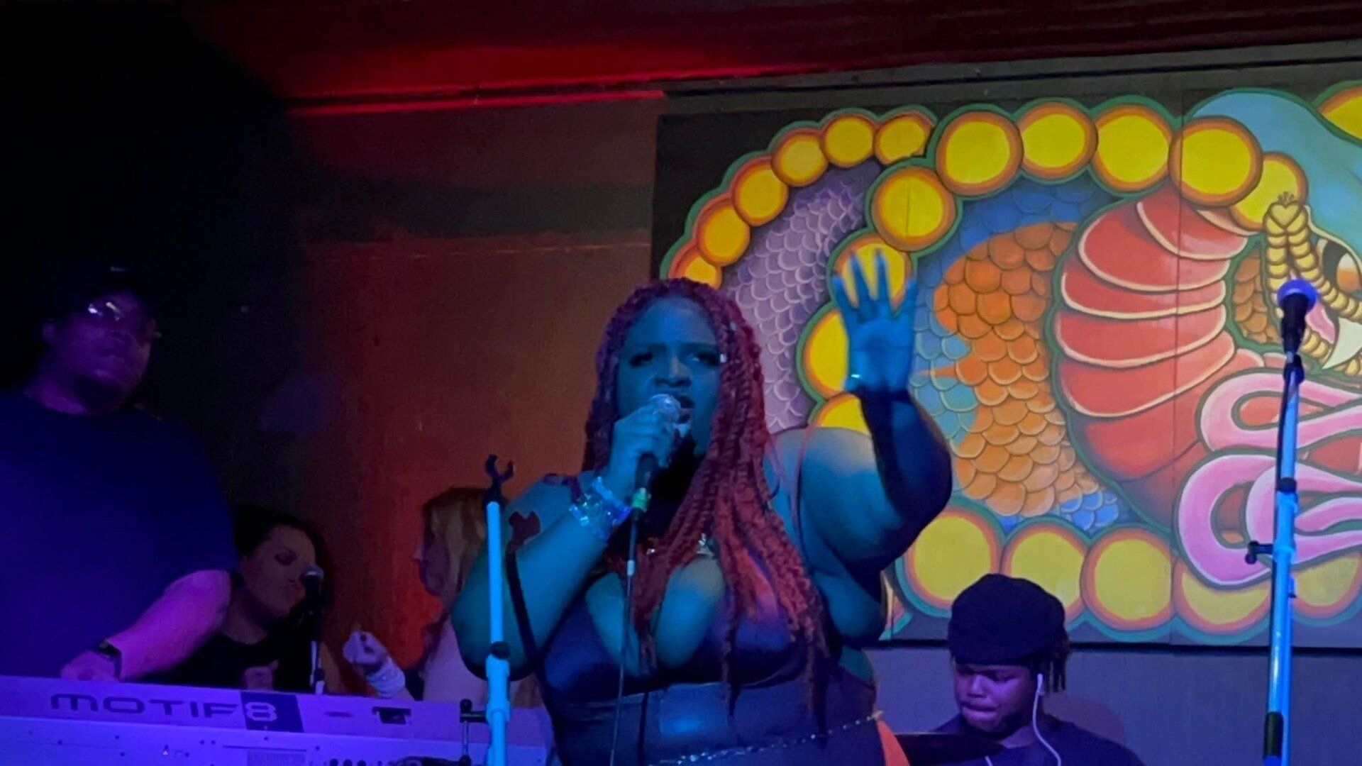 A woman is singing into a microphone on a stage in front of a painting.