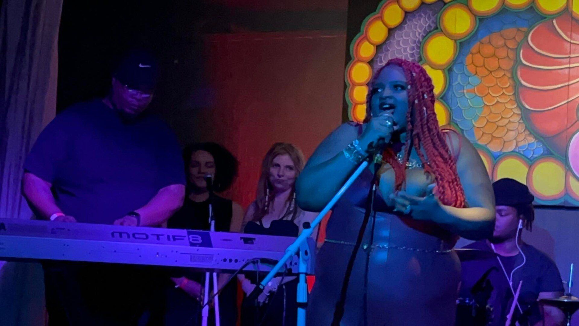 A woman is singing into a microphone on a stage while a man plays a keyboard.