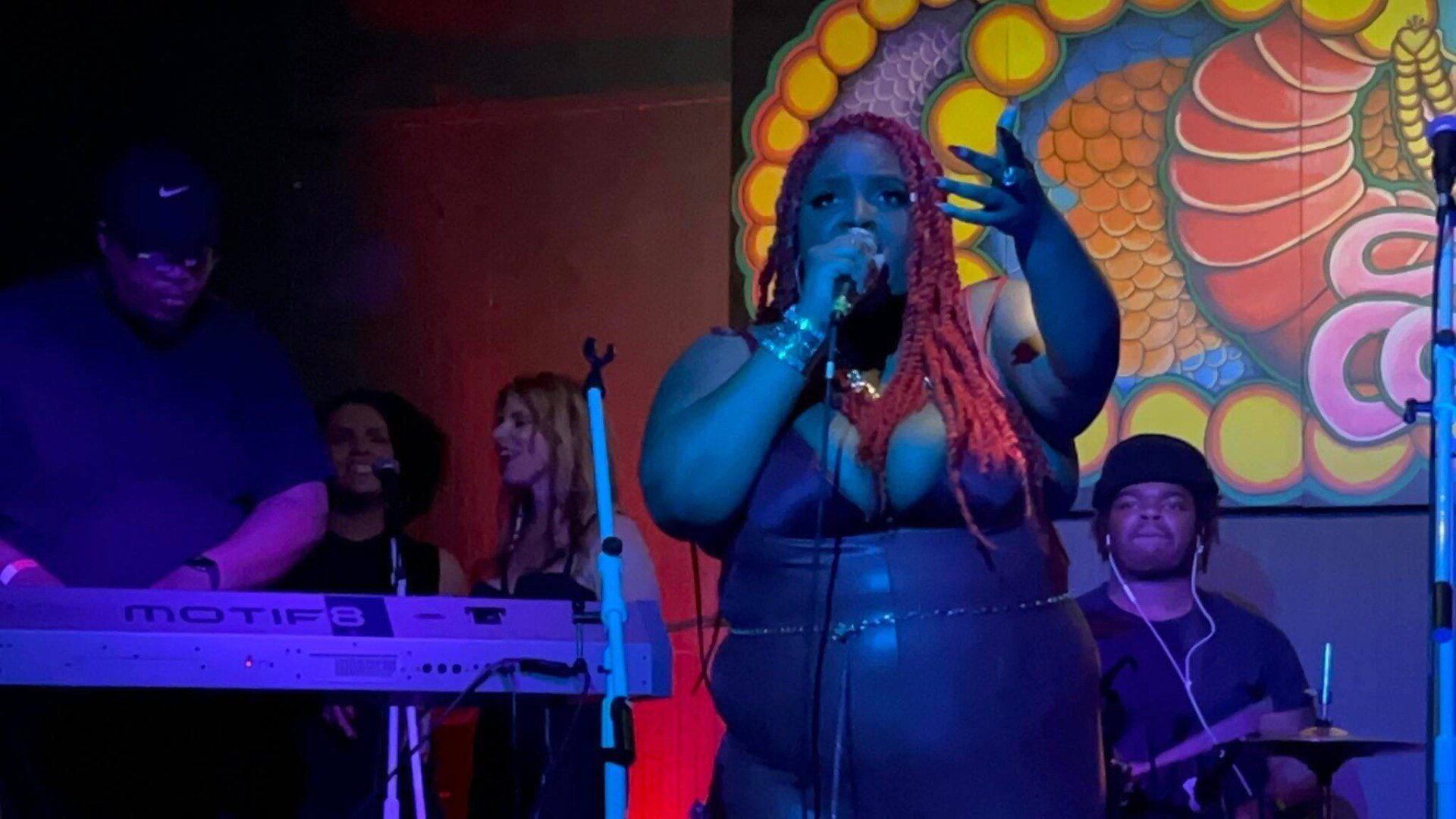 A woman is singing into a microphone on a stage while a man plays a keyboard.