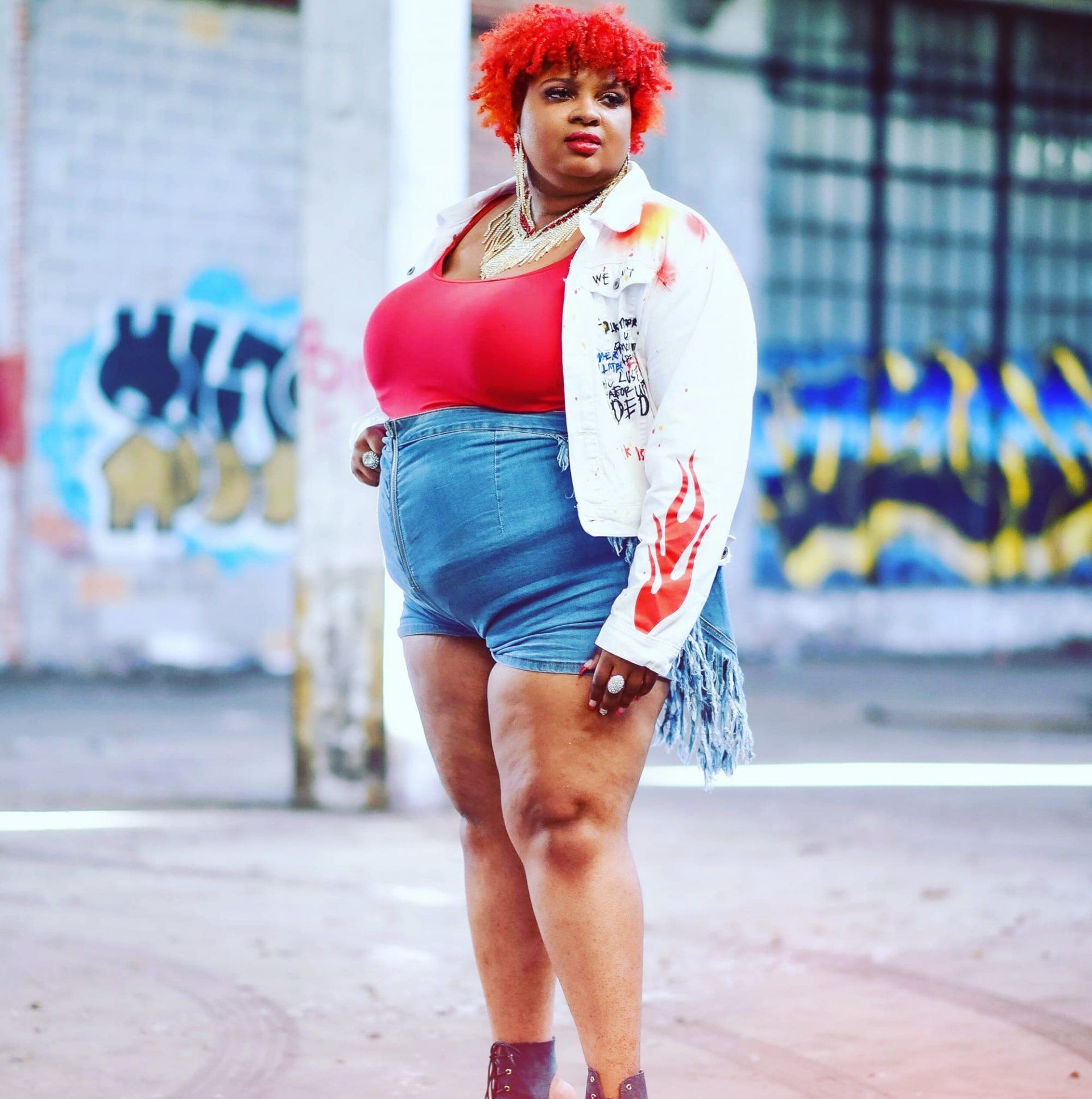 A woman with red hair is standing in front of a wall with graffiti on it
