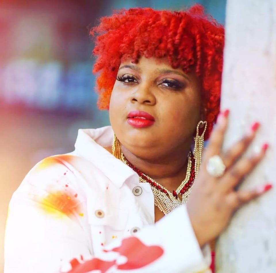 A woman with red hair is leaning against a wall.