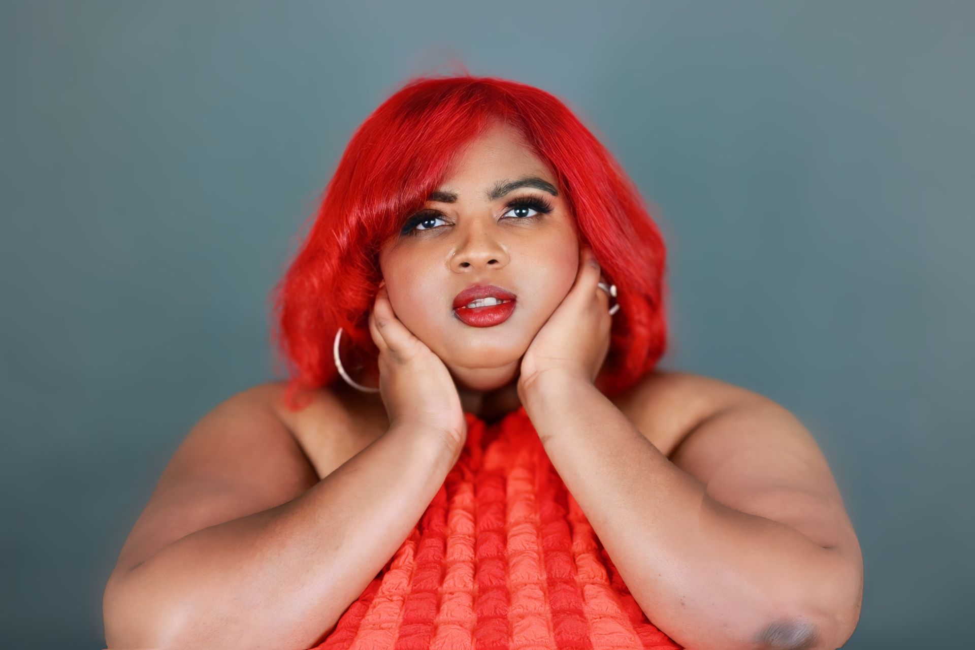 A woman with red hair is covering her face with her hands.