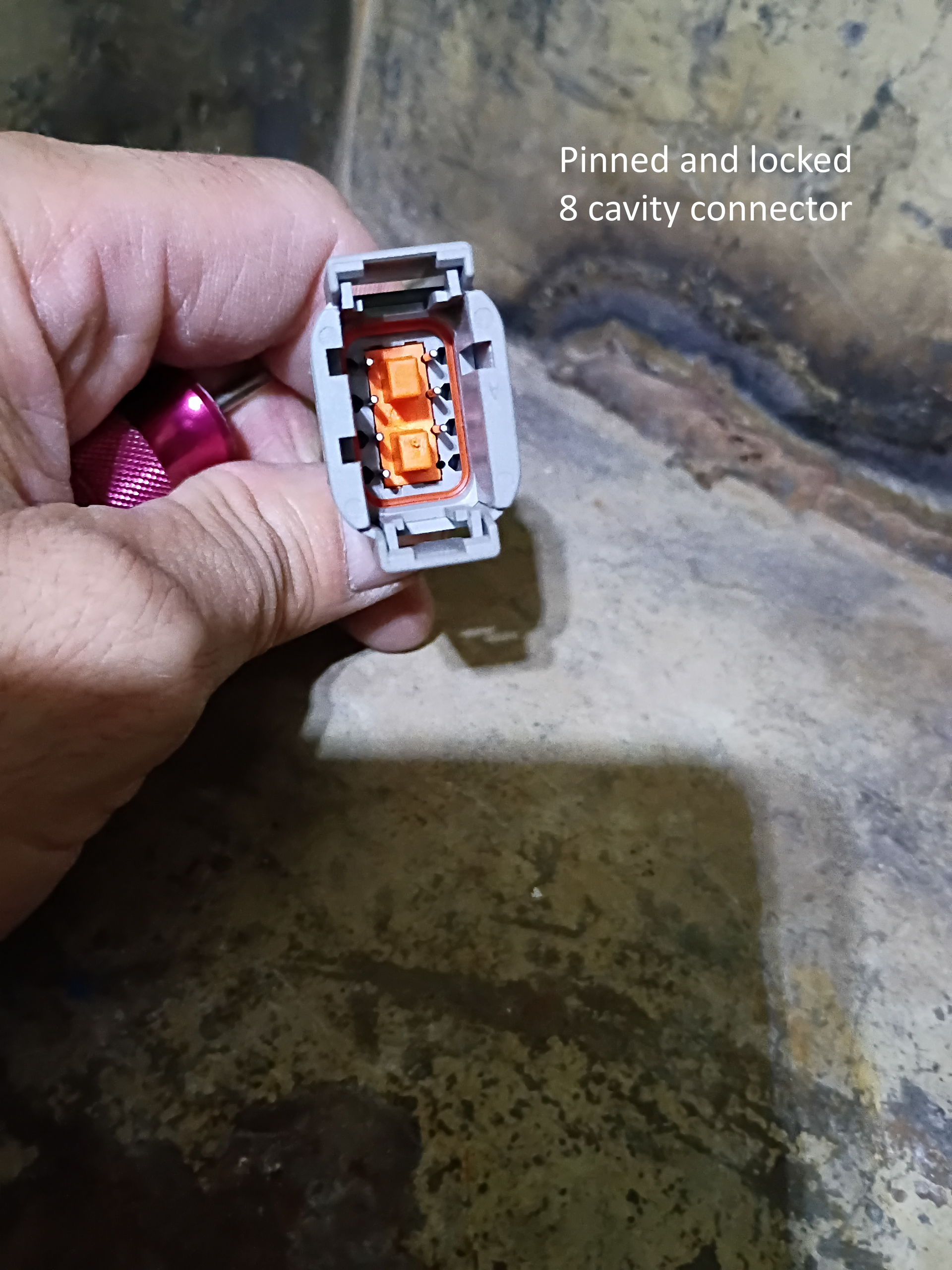 Hand holding a white and orange electrical connector against a concrete floor.