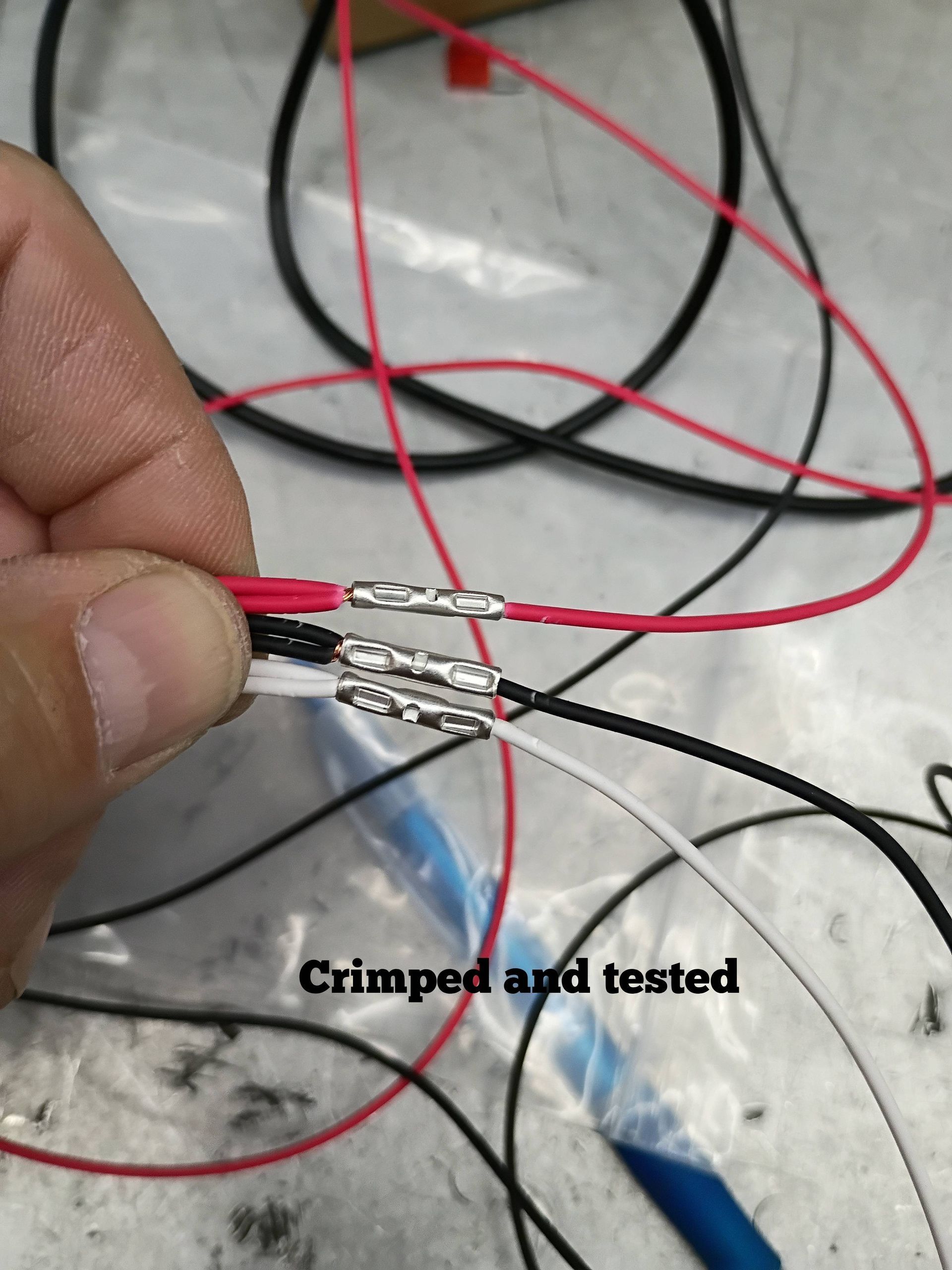 Hand holding crimped red, black, and white wires with exposed connectors on a light surface