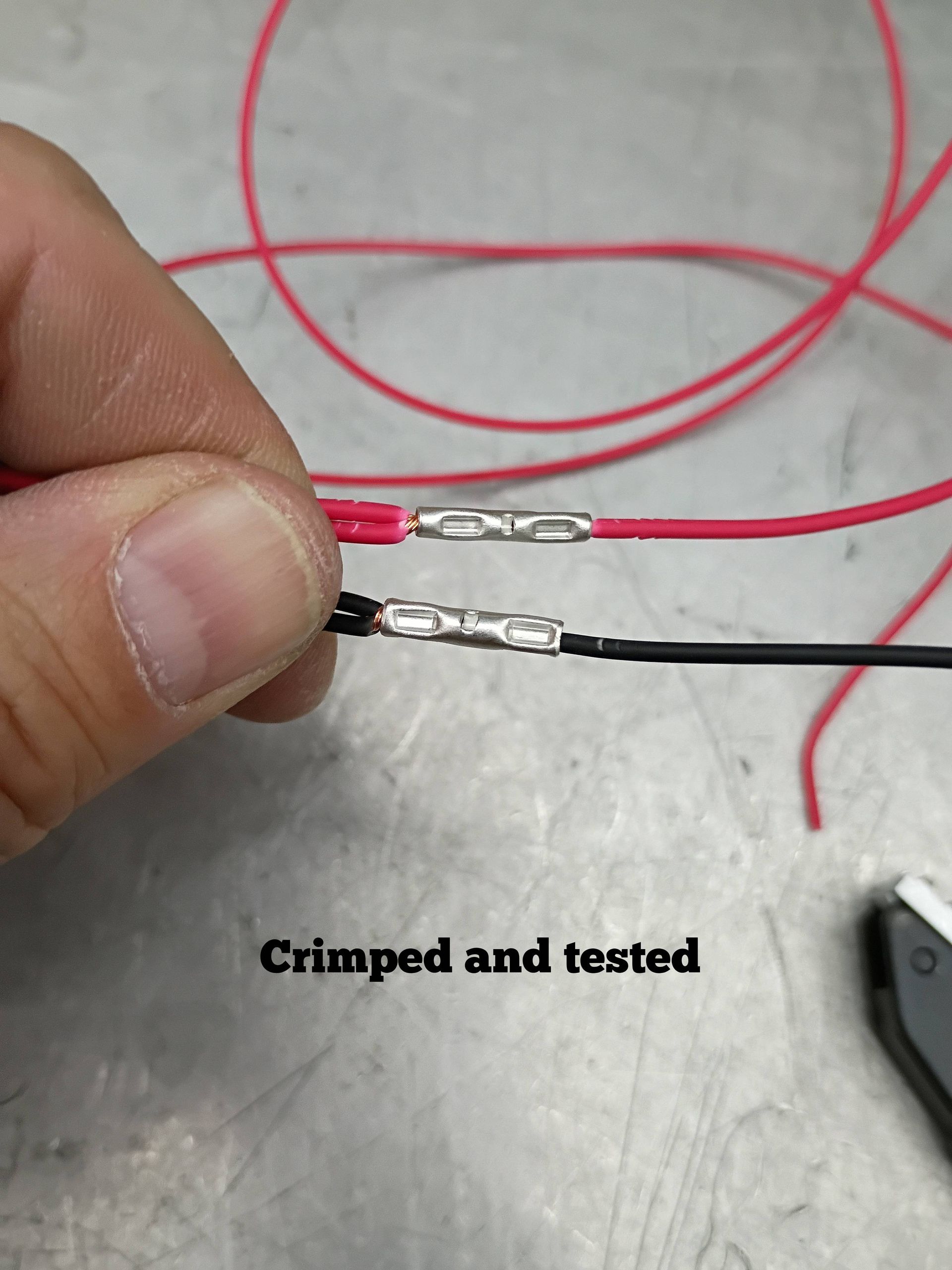 Close-up of crimped red and black wire connectors held by hand, with text reading “Crimped and tested”