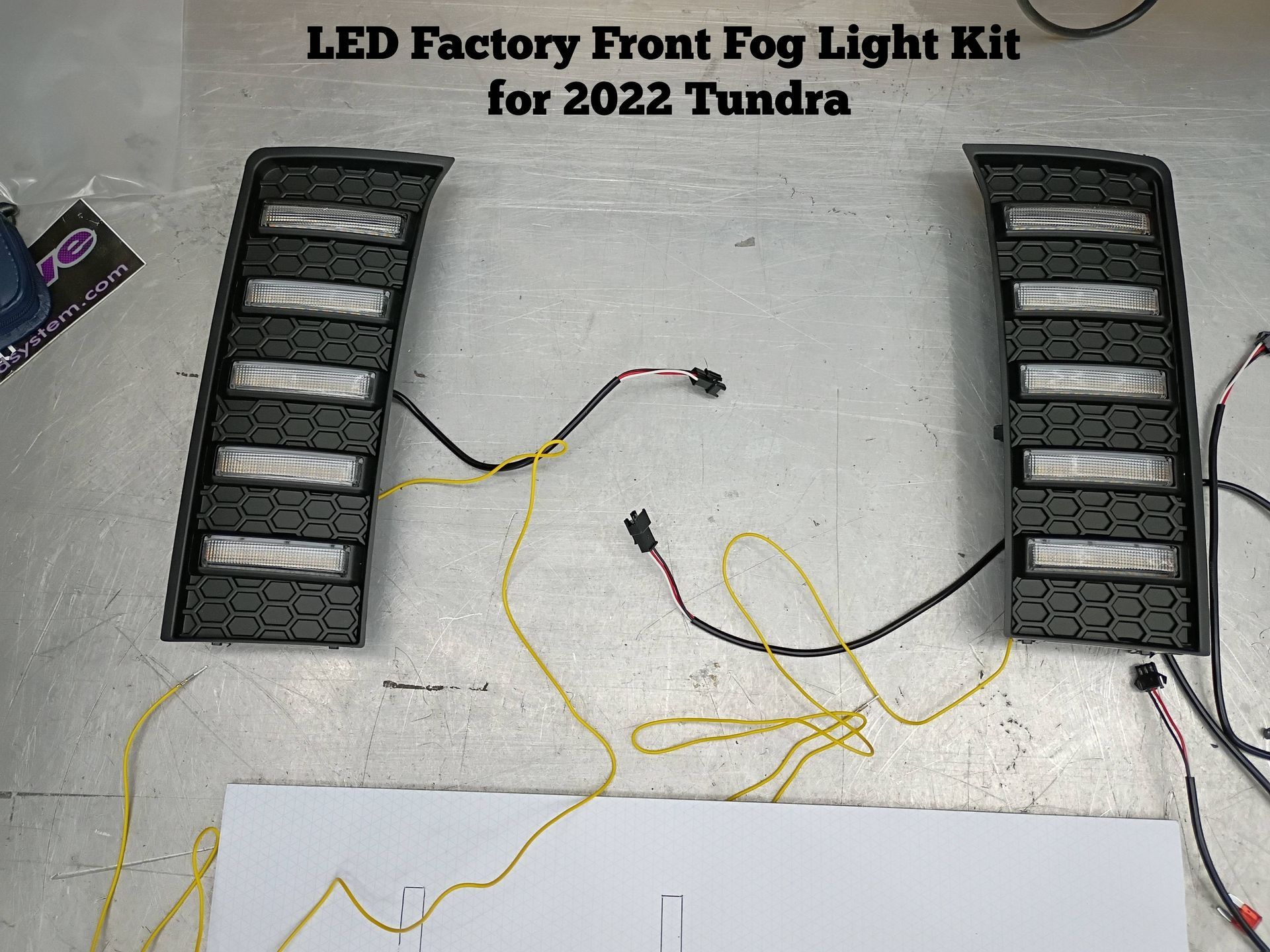 LED factory front fog light kit for 2022 Tundra, with two black light assemblies and yellow wiring on concrete floor