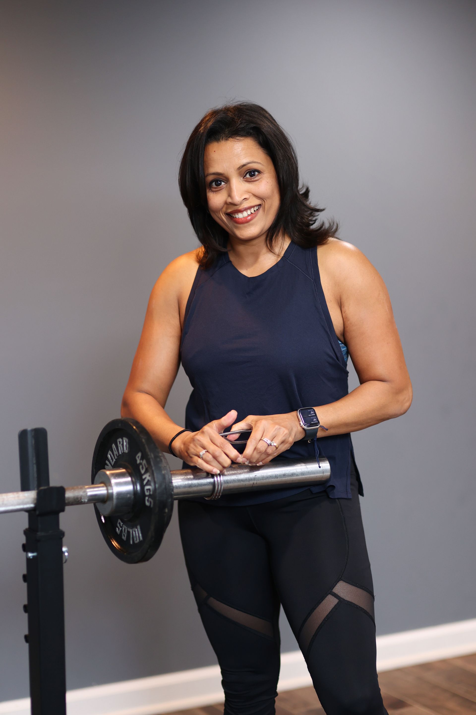 A woman is standing next to a barbell in a gym.