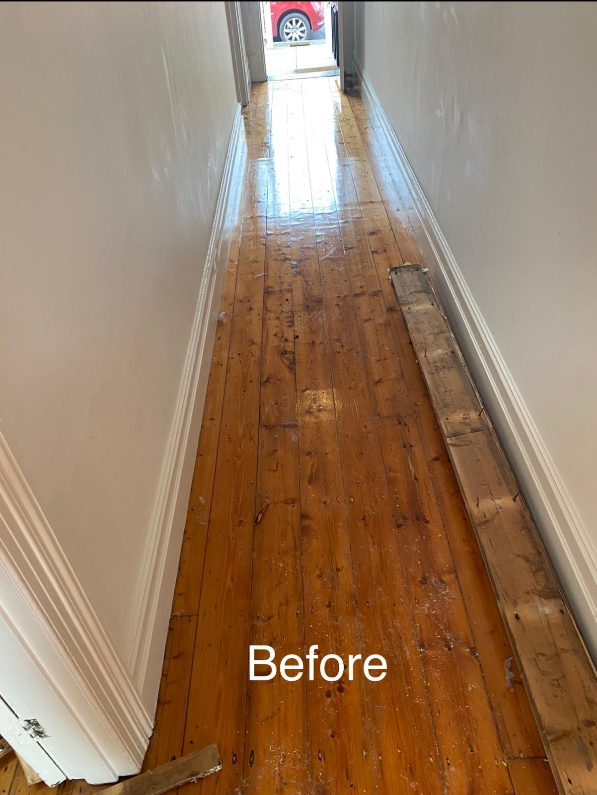 A hallway with wooden floors and a car parked in the background.