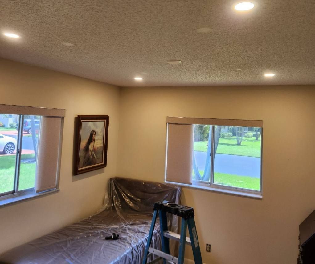 Bedroom with beige walls, recessed lights, two windows with shades, and a covered bed.