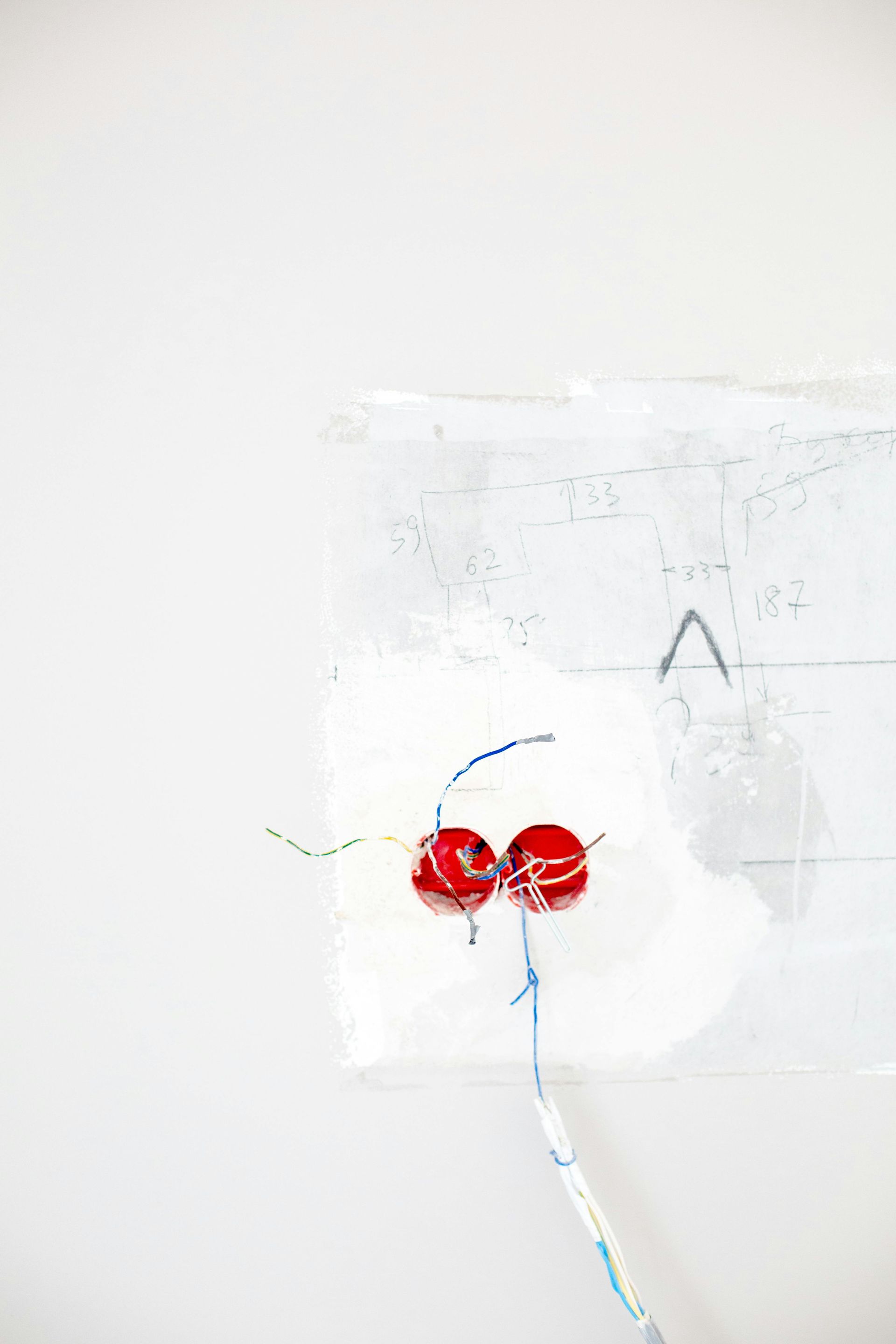 Two red electrical outlets with wires, in a white wall with spackle.