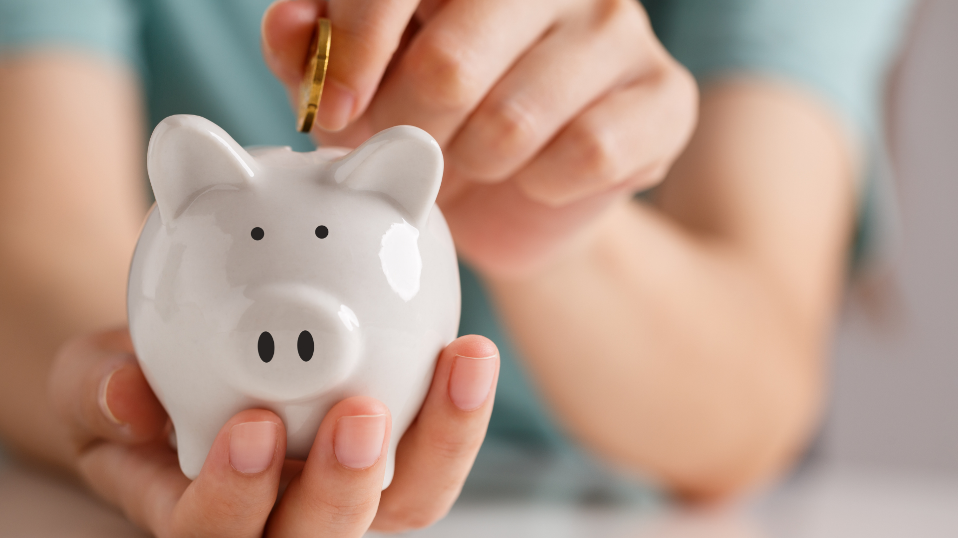 Hand placing a coin into a white piggy bank on a table