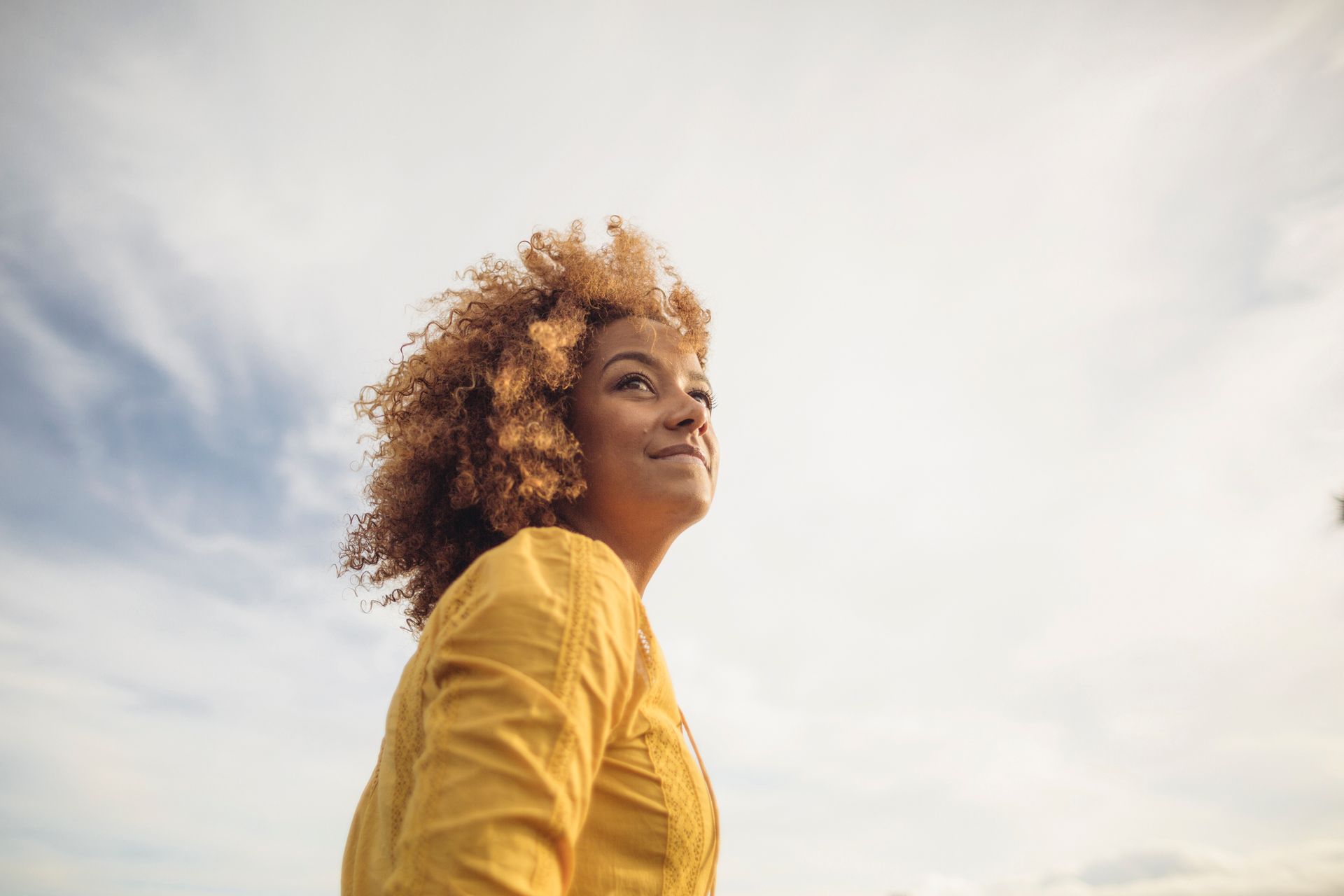 A woman in a yellow jacket is looking up at the sky.