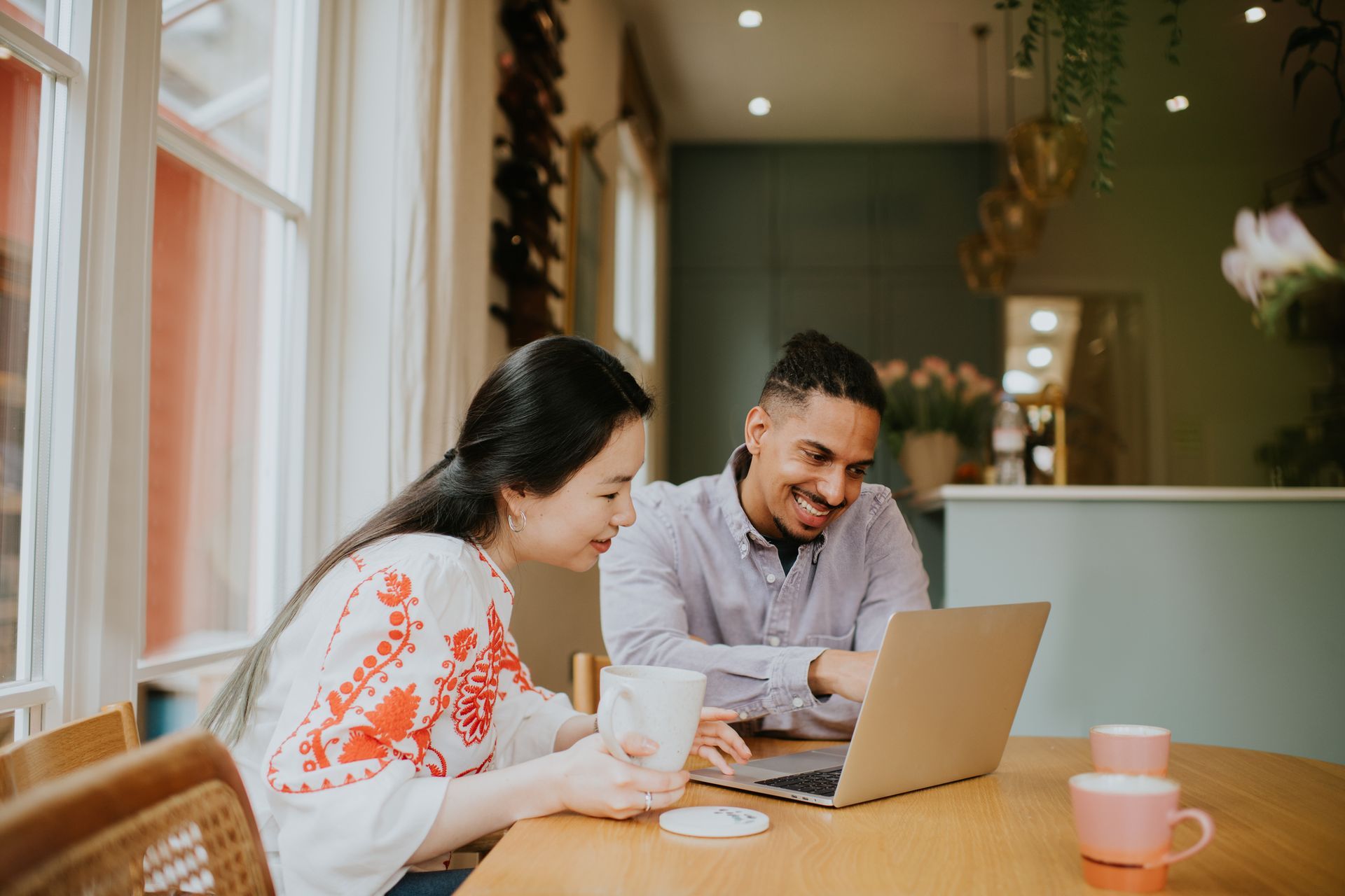 A man and a woman are sitting at a table looking at a laptop computer.
