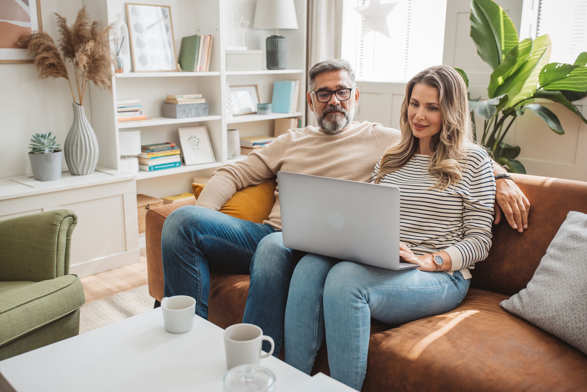 A man and a woman are sitting on a couch using a laptop computer.