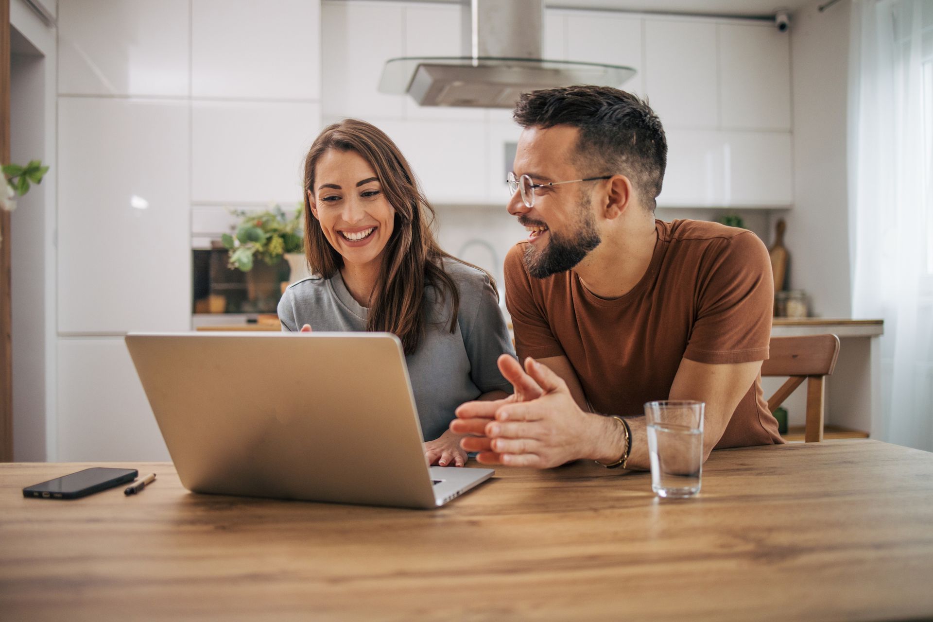 A man and a woman are sitting at a table looking at a laptop computer.