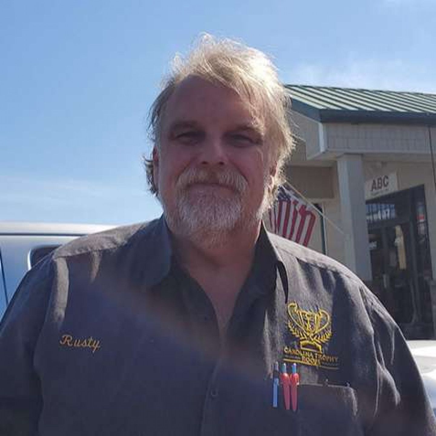 A man with a beard and the name rusty on his shirt