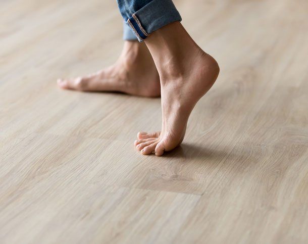 Side closeup view woman feet stands on warm wooden floor