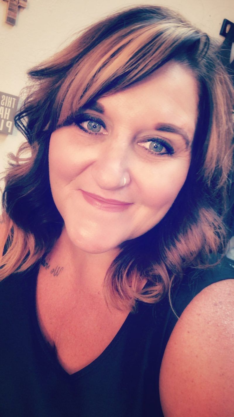 Close-up portrait of a smiling woman with wavy brown hair and a nose ring, wearing a black top.