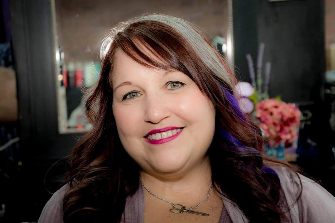 Smiling woman with long brown hair and pink lipstick in a softly lit indoor setting