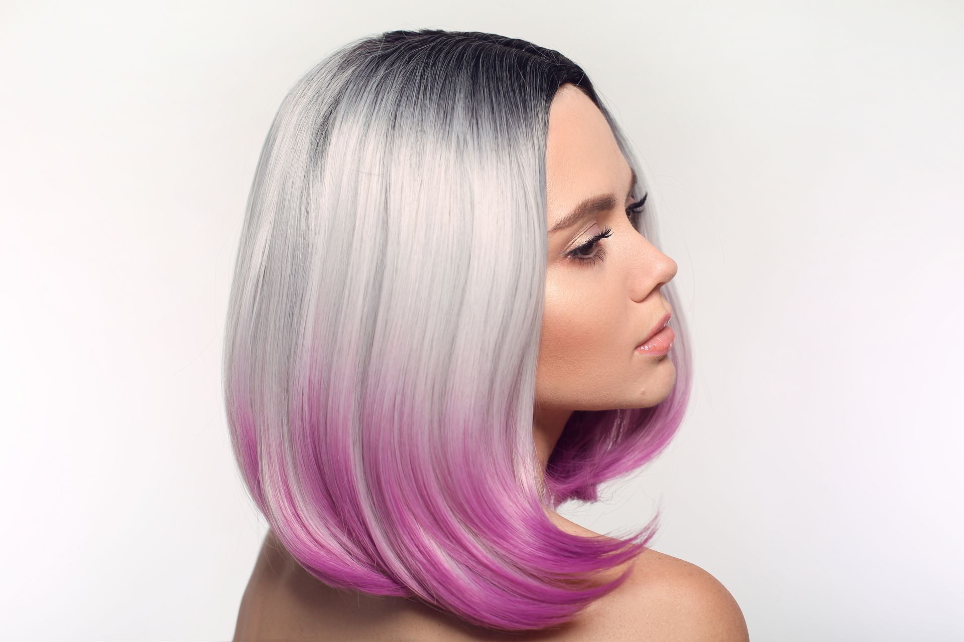 Woman with sleek silver bob fading to pink at the ends, shown in profile on a plain background