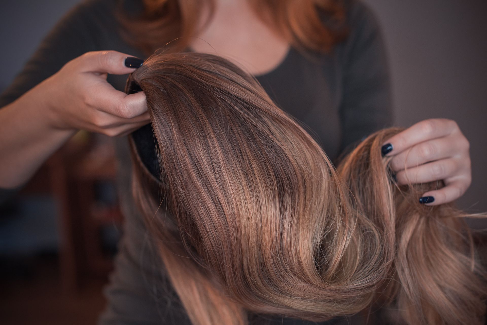 Hands holding and displaying long, wavy light-brown hair indoors