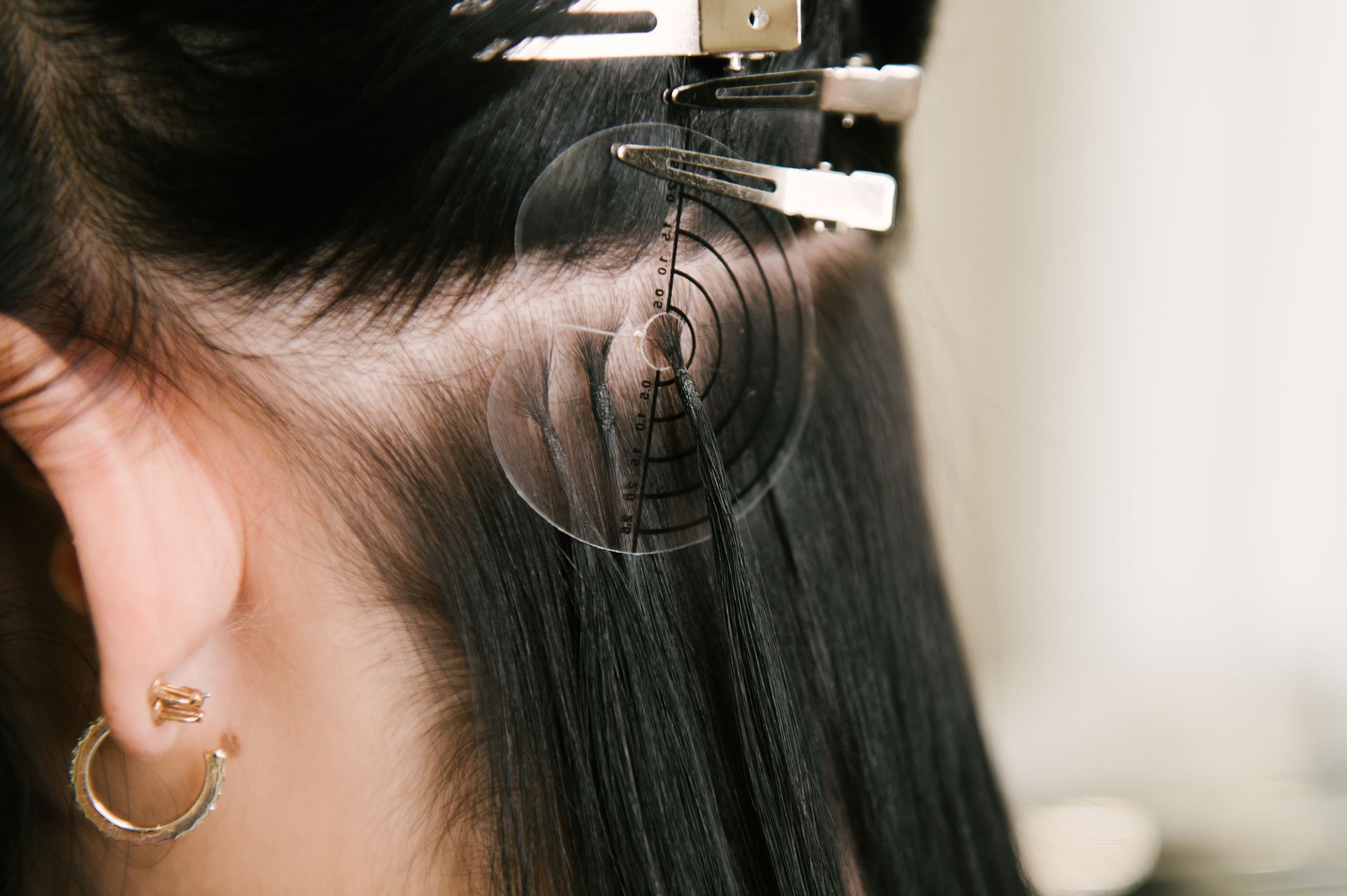 Close-up of hair extensions being attached with a clip-on tool at a salon.