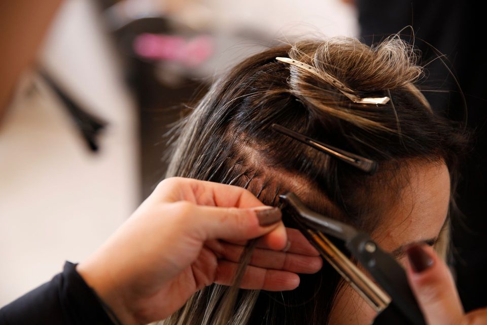 Stylist curling a woman’s dark hair with a curling iron in a salon