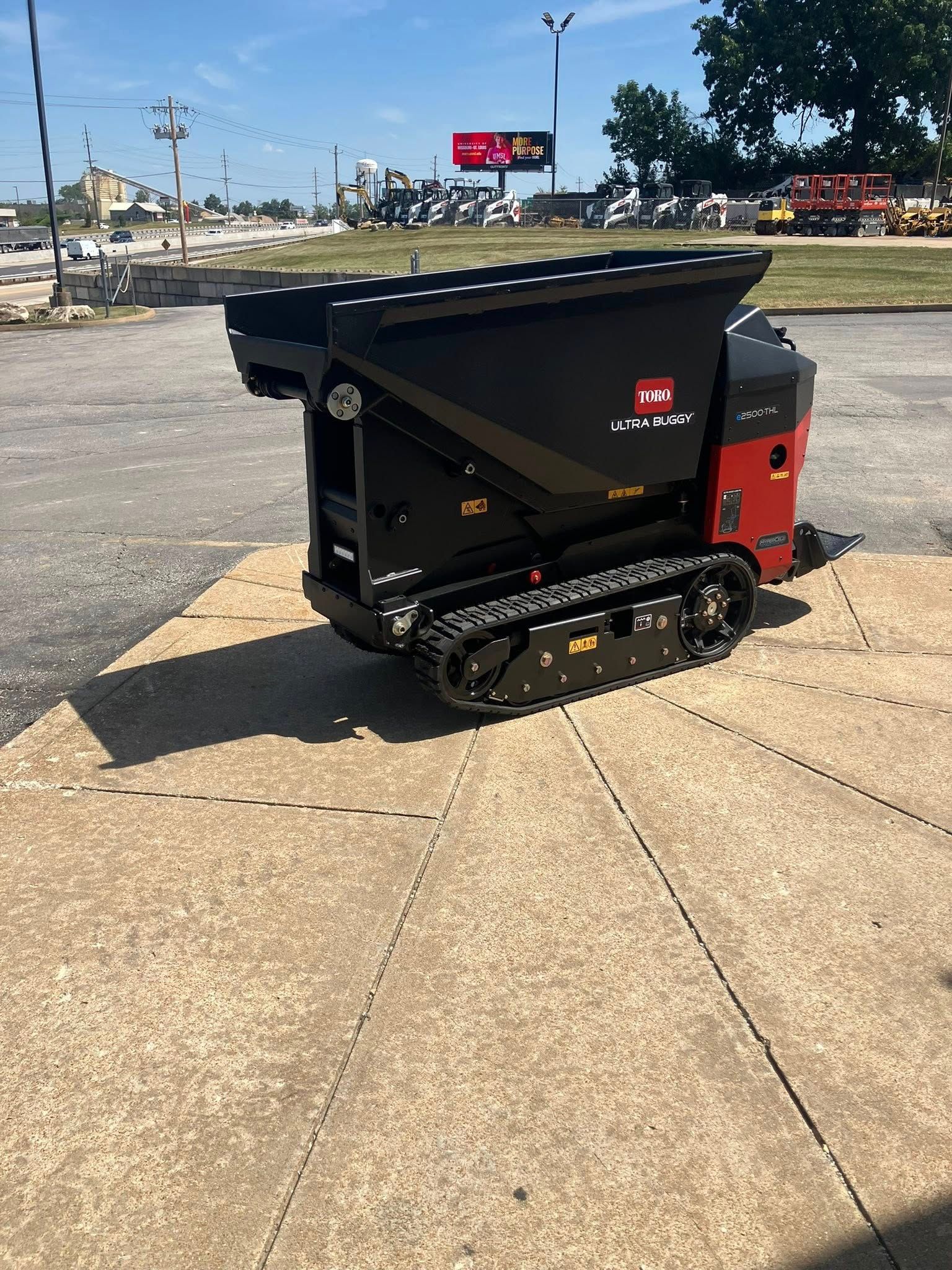 A black and red tracked power buggy parked on a concrete lot on a sunny day.