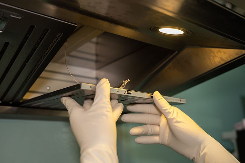 Una persona che indossa guanti bianchi sta pulendo la cappa di una cucina.