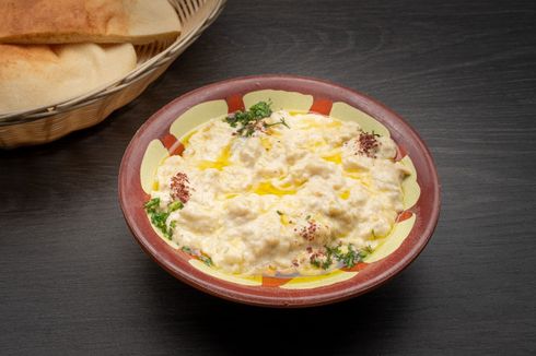 baba ghanough A bowl of baba ghanough is on a table next to a basket of pita bread.