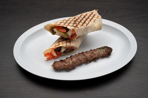 Beef Kofta Sandwich A white plate topped with a wrap and a skewer of meat.