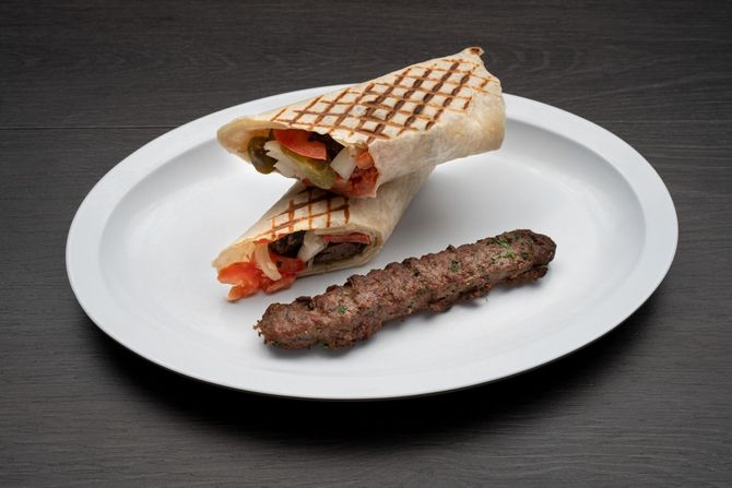 Beef Kofta Plate A white plate topped with a wrap and a skewer of meat.