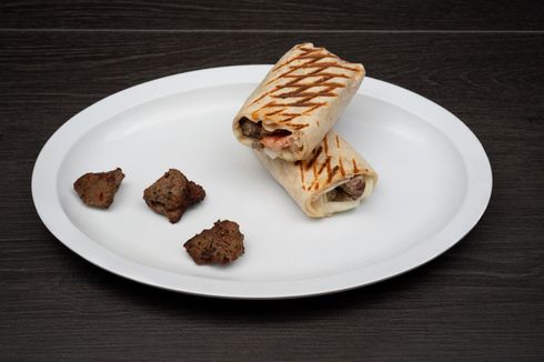 A white plate topped with a burrito and some meat