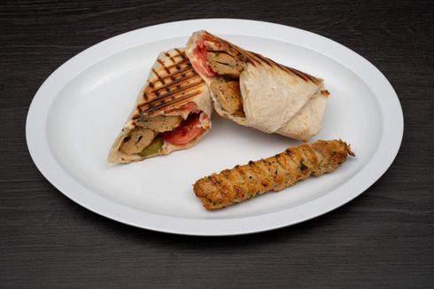Chicken Kofta A white plate topped with a sandwich and a chicken kofta on a table.