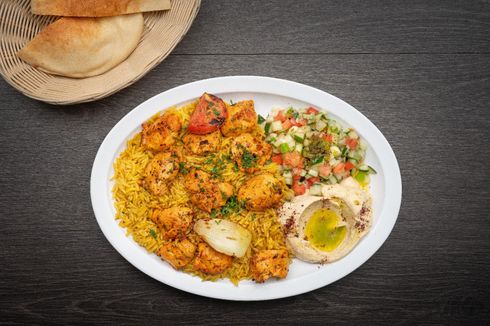 Chicken Tawook Plate A plate of food with rice , chicken , hummus and pita bread on a table.