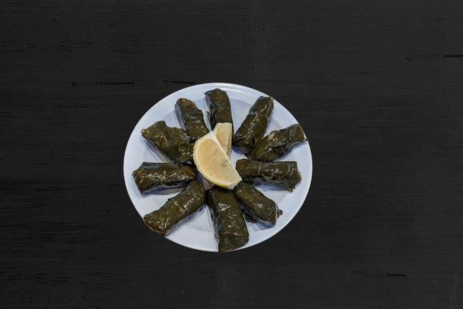 Dolma A white plate topped with stuffed grape leaves and a slice of lemon
