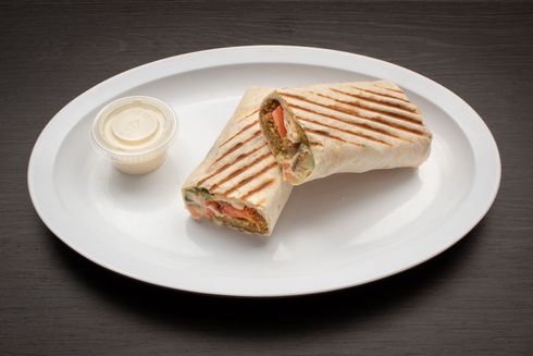 Falafel Sandwich A white plate topped with a falafel sandwich and a dipping sauce.
