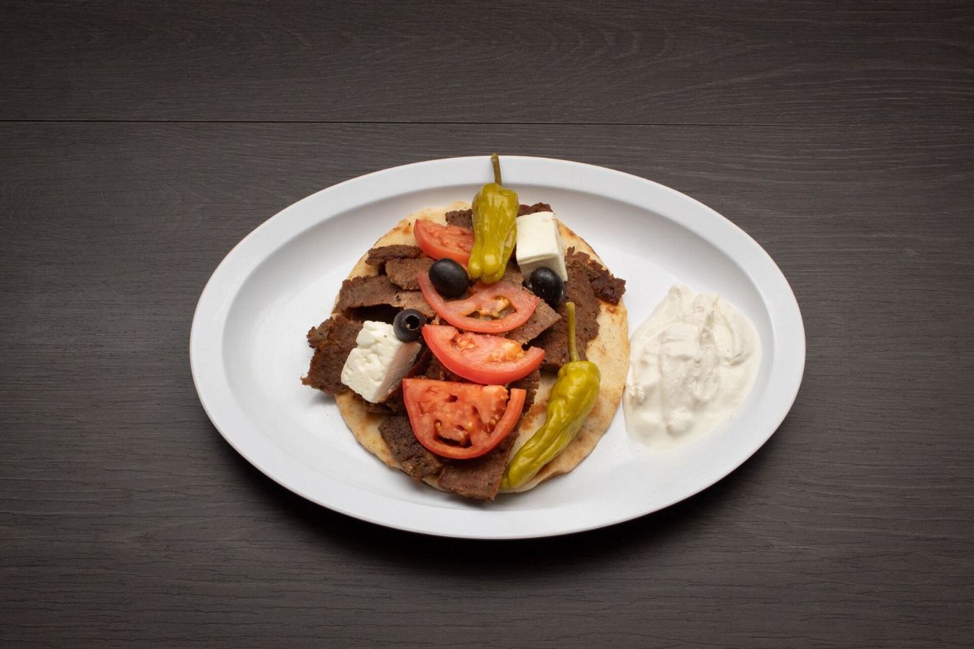 Gyro Sandwich A white plate topped with a gyro with tomatoes and peppers